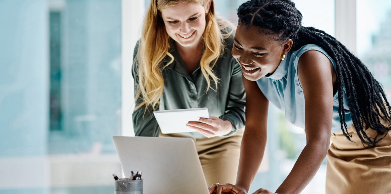 Two people smiling whiling looking at a laptop computer in a modern office